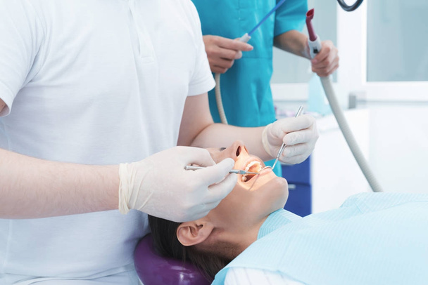 Una mujer está sentada en una silla dental en la recepción de un dentista. Un médico masculino está tratando los dientes del paciente.
. - Foto, Imagen