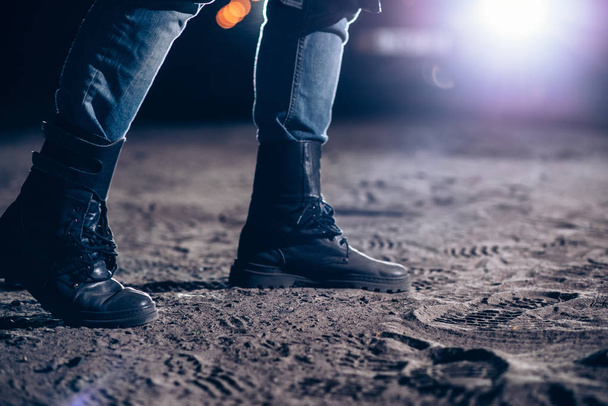  closeup of man wearing leather boots at night, car lights on background. Horror, murderer concept - Photo, Image