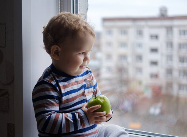 窓辺に緑のリンゴを食べる少年 - 写真・画像