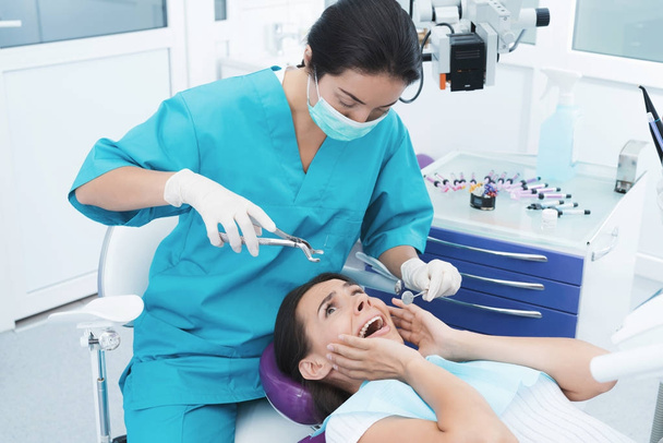 A female dentist is treating a patient. She sits on the dental chair and is afraid. - Foto, Imagen