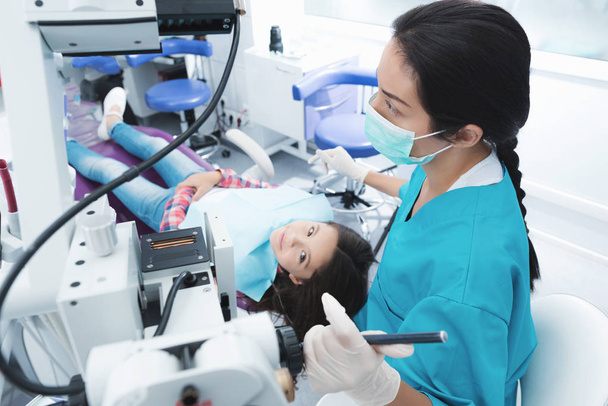 A female dentist is treating a girl. She sits on the dental chair and smiles. - Photo, Image