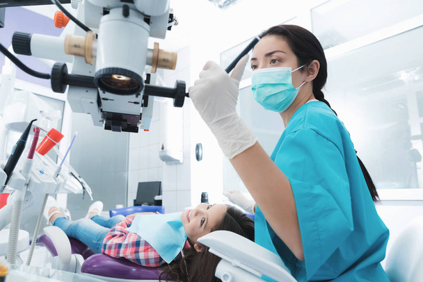 A female dentist is treating a girl. She sits on the dental chair and smiles. - Фото, изображение