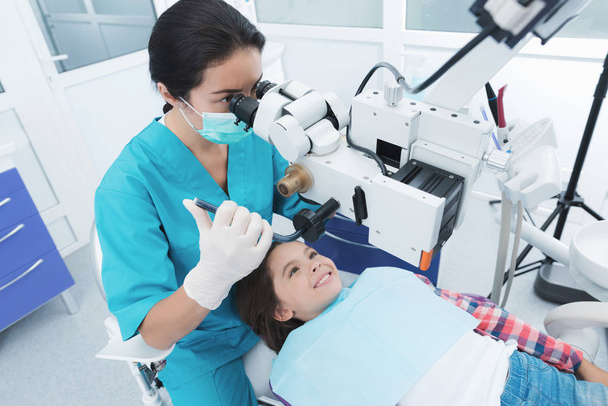 A female dentist is treating a girl. She sits on the dental chair and smiles. - Foto, Bild