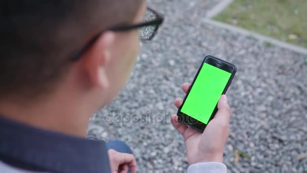 Ένας νεαρός άνδρας με ένα τηλέφωνο με μια πράσινη οθόνη - Πλάνα, βίντεο