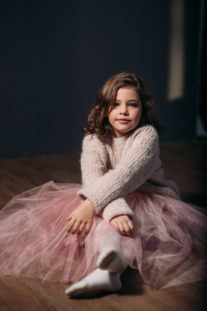 Little beautiful girl with brown hair in a light sweater and a skirt of tulle. Studio. A princess poses for a photographer. - Foto, Bild