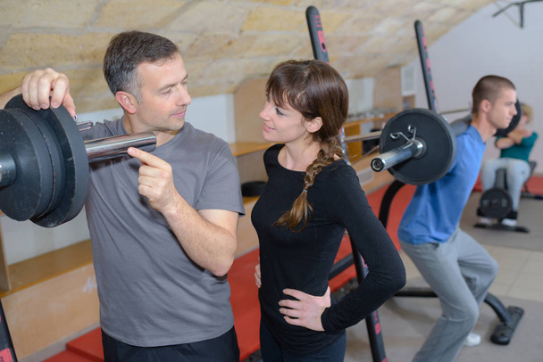 Trainer erklärt, wie man ein Trainingsgerät im Fitnessstudio einsetzt - Foto, Bild