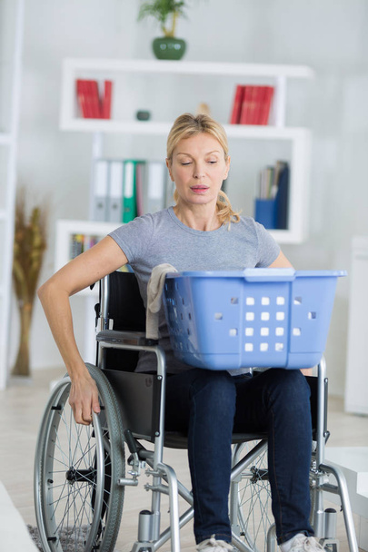 young happy woman on wheelchair putting clothes in basket - Фото, изображение