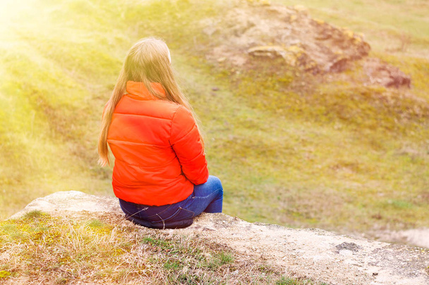 Девушка в красной куртке сидит на вершине горы
. - Фото, изображение