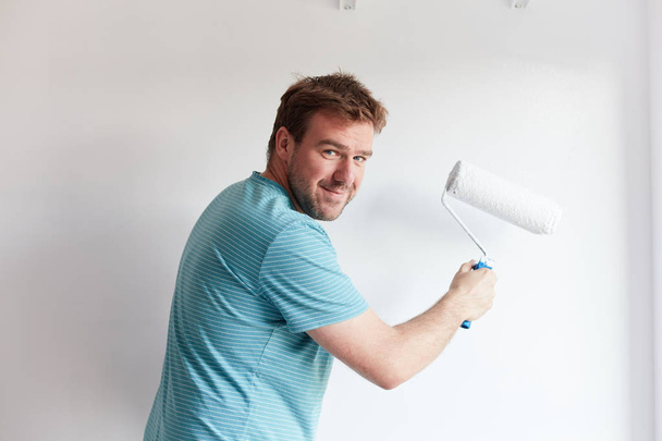 Jeune homme peignant un mur sur blanc dans une maison moderne
 - Photo, image