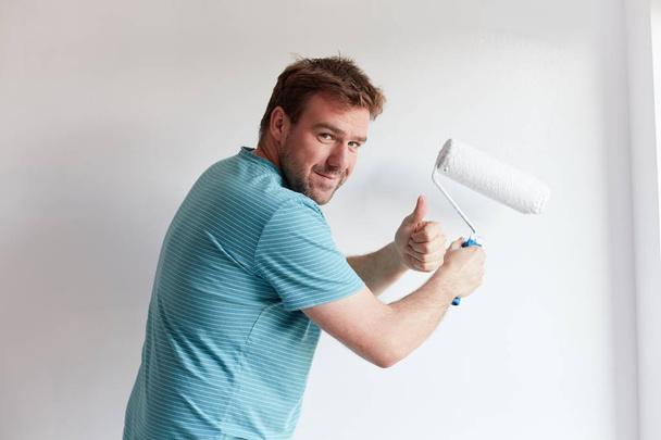 Νεαρός άνδρας βάψετε έναν τοίχο σε λευκό, σε ένα σύγχρονο σπίτι - Φωτογραφία, εικόνα