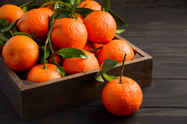 Čerstvé mandarinky klementinky s listy v dřevěný zásobník na tmavé dřevěné pozadí. - Fotografie, Obrázek