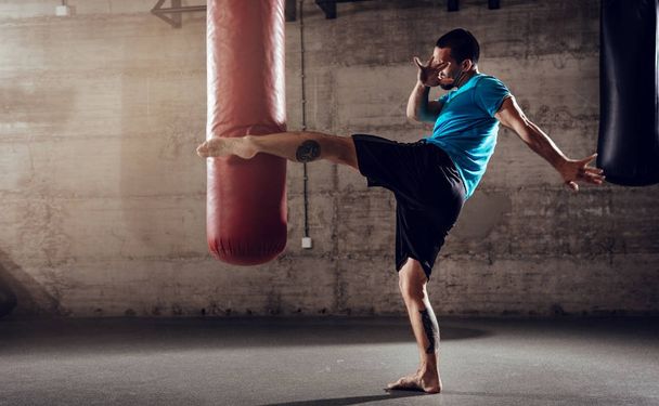 Мужчина бьет ногой боксерскую сумку
  - Фото, изображение