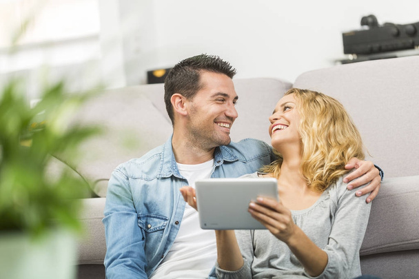 Relaxado jovem casal usando um tablet em sua sala de estar
 - Foto, Imagem