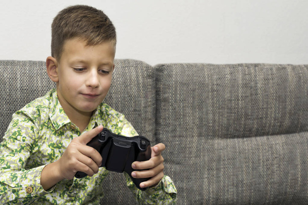 Boy playing video games with joystic sitting on sofa - 写真・画像