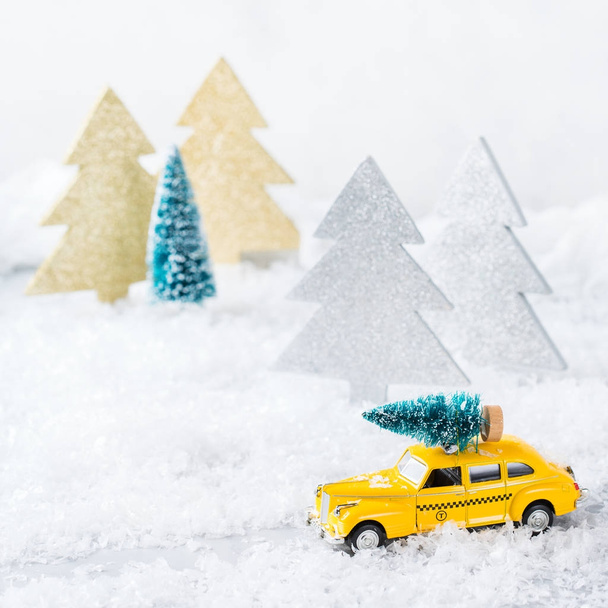 Újévi ünnepi koncepció. Sárga játék taxi autó szállító karácsonyfa egy hóerdőben. Fénymásolás tér üdvözlő kártya ünnepi dekoráció - Fotó, kép