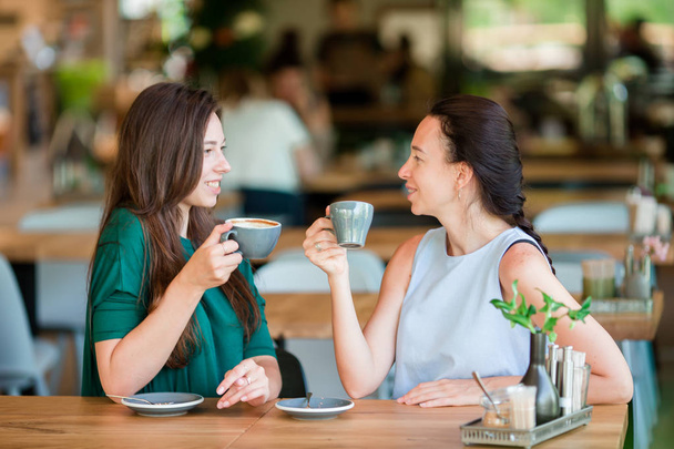 Gelukkig jonge vrouwen met kopjes koffie op het terras. Communicatie en vriendschap concept - Foto, afbeelding