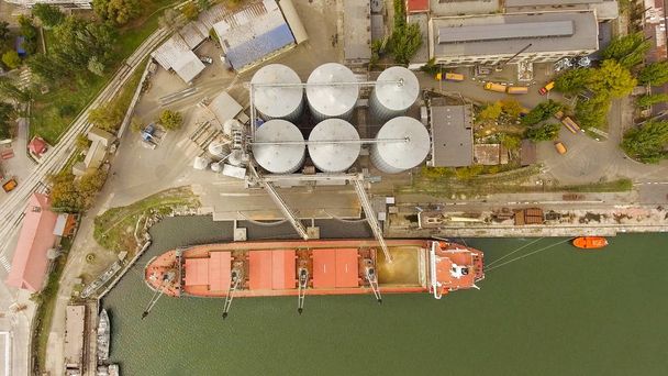 Вид с воздуха на большие зерновые элеваторы на море. Погрузка зерна на корабль. Порт. Грузовой корабль
 - Фото, изображение