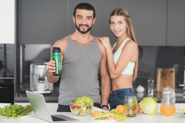 Un hombre y una mujer en la cocina por la mañana. Un hombre jugará con un cóctel de verduras verdes en sus manos.
. - Foto, Imagen