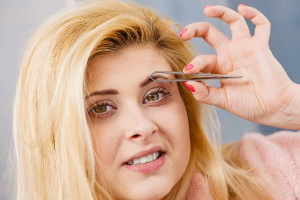 Woman tweezing eyebrows depilating with tweezers - 写真・画像