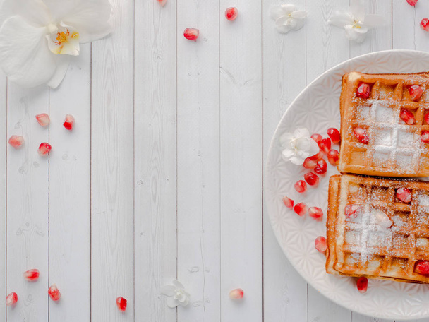 Delicious mouth-watering Viennese waffles with honey and pomegranate seeds on a white plate, light wooden background Copy space - Φωτογραφία, εικόνα