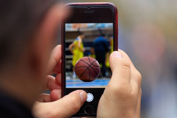 Basket ball immagine appare su tablet, smartphone nelle mani dell'uomo. Sfondo sfocato
 - Foto, immagini