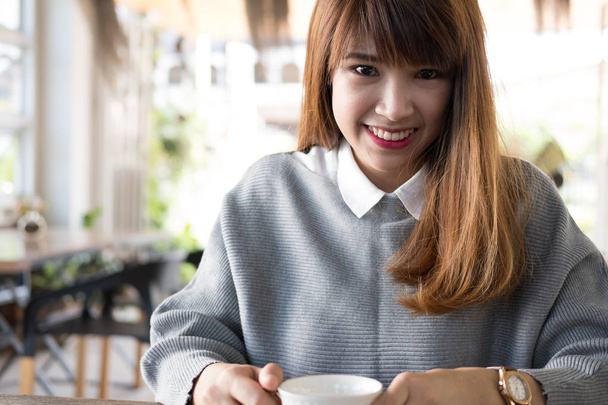 vrouw zitten in café met warme cappuccino koffie op houten tafel durin - Foto, afbeelding