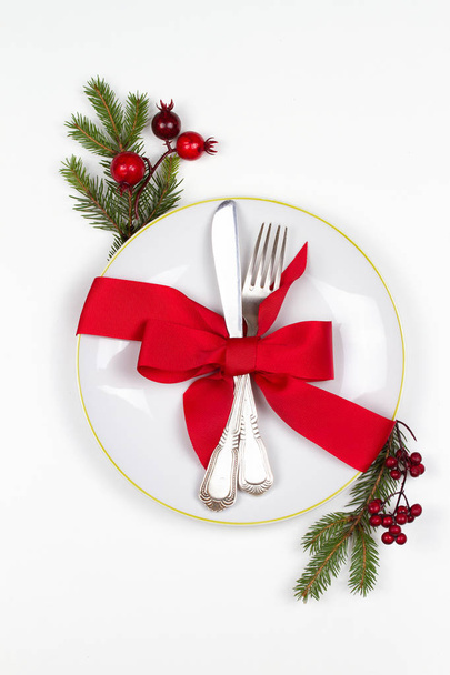Christmas table place setting with plate, cutlery, pine branches,  ribbon and red berries. Winter holidays and festive background. Christmas eve dinner, New Year food lunch - 写真・画像