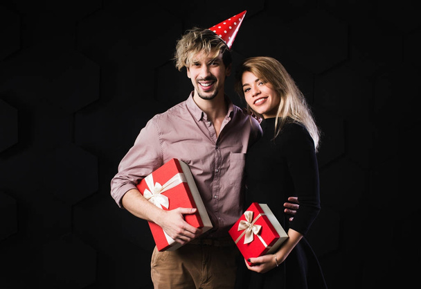 Happy couple hold red presents box, man and woman smile looking at camera embracing, on black background. - Foto, afbeelding