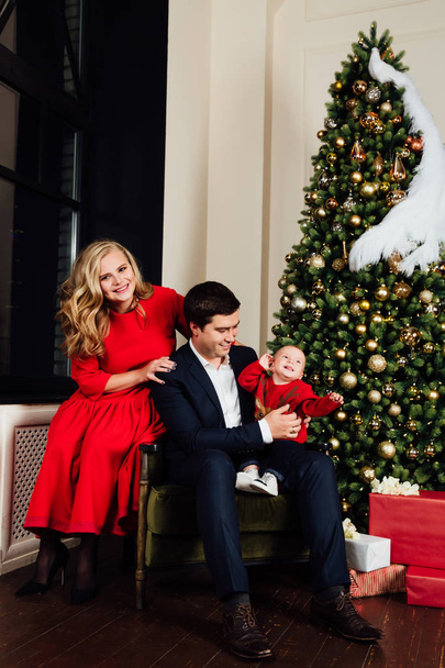 Portrait of a family on a christmas tree background. Mom, Dad and a one-year-old baby boy. - Foto, afbeelding