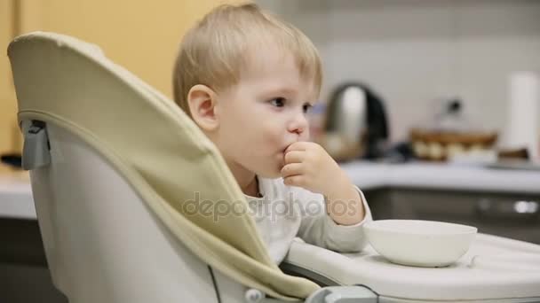 Mały chłopiec siedzi w foteliku w kuchni i z płyt jest bardzo smaczne jedzenie. Uśmiecha się i gra. - Materiał filmowy, wideo