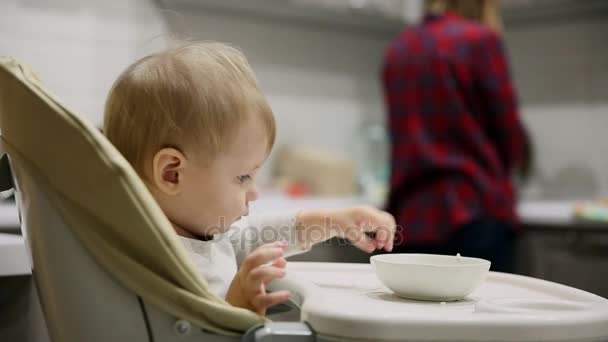 Pieni poika istuu lastenistuimella keittiössä ja lautasilta on erittäin maukasta ruokaa. Hymyjä ja näytelmiä
. - Materiaali, video
