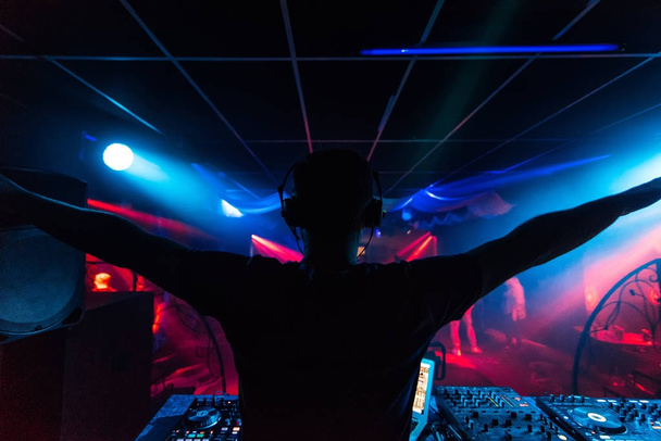 DJ kulaklıklar renkli ışık ile parti gece kulüp silüeti kollarını sallayarak - Fotoğraf, Görsel