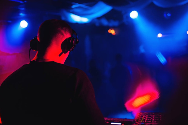 DJ mit Kopfhörer am Mischpult spielt Musik in Nachtclub-Silhouette - Foto, Bild