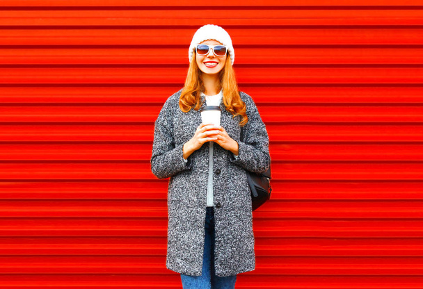 Fashion smiling woman with coffee cup wearing a coat on a red ba - Foto, Bild