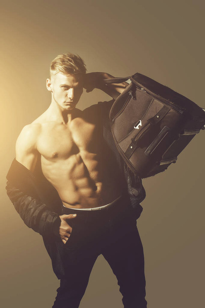 gespierde man met sexy lichaam houdt grote zak, koffer - Foto, afbeelding