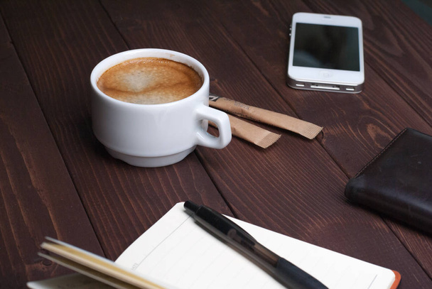 Smartphone with notebook and cup of strong coffee on wooden background - Fotó, kép