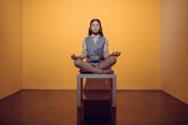 asian businesswoman meditating on table in front of orange wall - Photo, Image