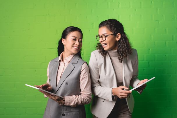 african american and asian businesswomen working with digital tablets in front of green wall - Фото, изображение