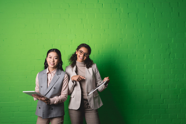 alegre africano americano y asiático businesswomen trabajando con digital tablets en frente de verde pared
 - Foto, imagen