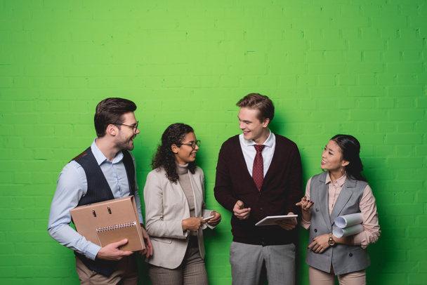 nuoret monikansalliset liikemiehet, joilla on digitaaliset laitteet ja asiakirjat vihreän muurin edessä
 - Valokuva, kuva