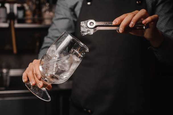 Barman in the apron putting ice cubes into the cocktail glass - Фото, зображення