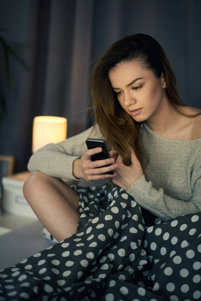 Young beautiful woman using phone while laying in bed  - Photo, Image
