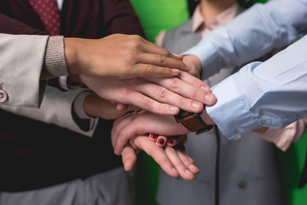 cropped view of business team holding hands together in front of green wall - Photo, Image
