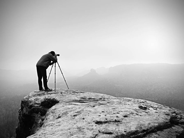 Hiker with camera on tripod takes picture from rocky summit. Alone photographer  on summit - Photo, Image