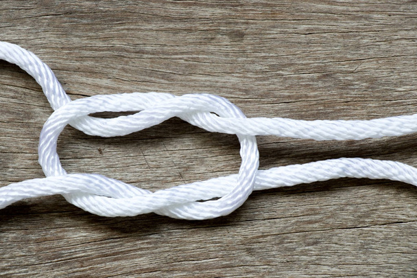 White rope in reef knot shape on wood background - Zdjęcie, obraz