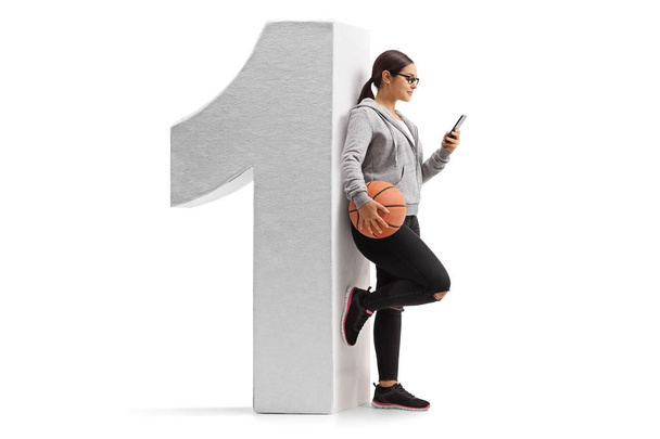 meisje met een basketbal en een telefoon leunend tegen een nummer een - Foto, afbeelding
