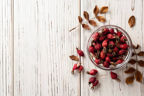 Dried rose hips in glass bowl on white wooden background - Zdjęcie, obraz