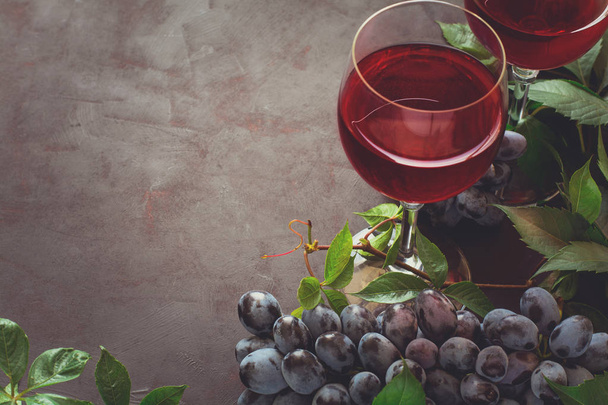 Still life with wineglasses, bottles, grapes and leaves on brown wooden desk - Foto, Imagem