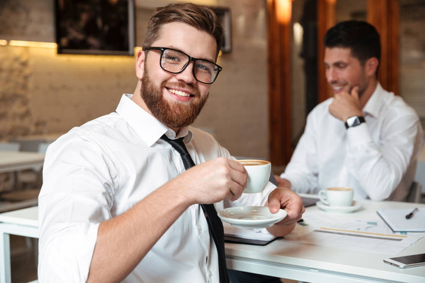 Портрет улыбающегося бородатого бизнесмена, пьющего кофе
 - Фото, изображение