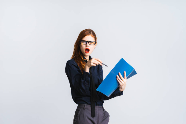 dissatisfied evil red-haired girl with glasses and a blue shirt is holding documents in her hands and pointing at them - Фото, изображение